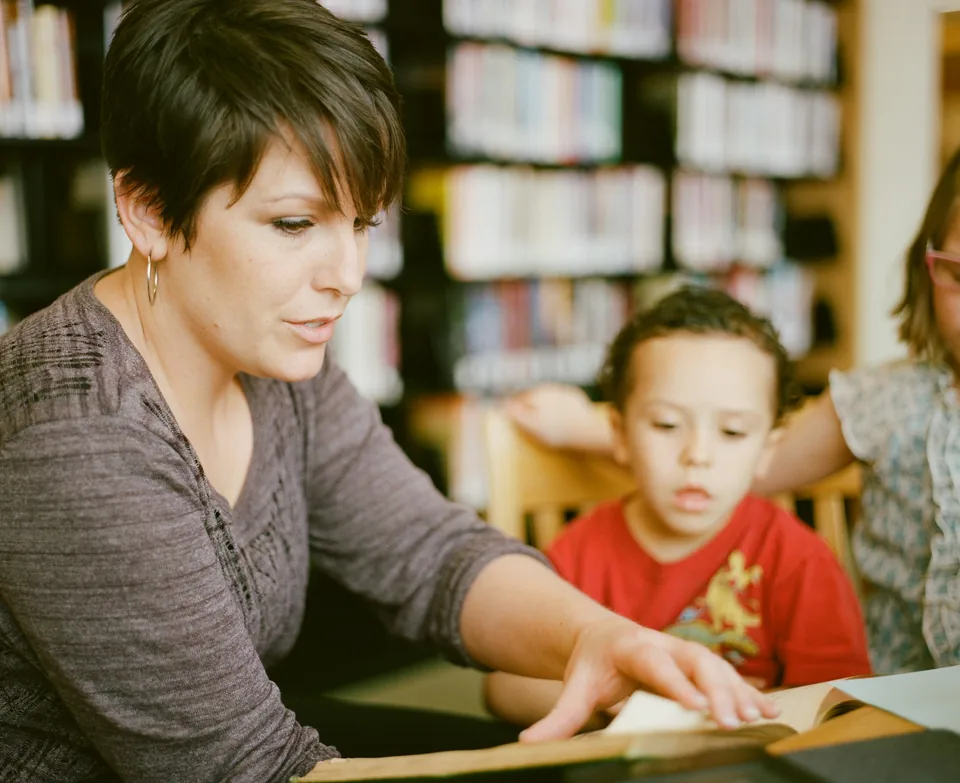 An adult reading a book with children at a library table