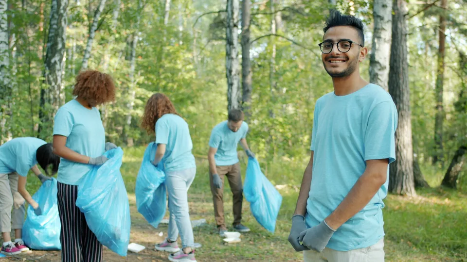 People wearing gloves collecting litter with blue bags in a wooded park