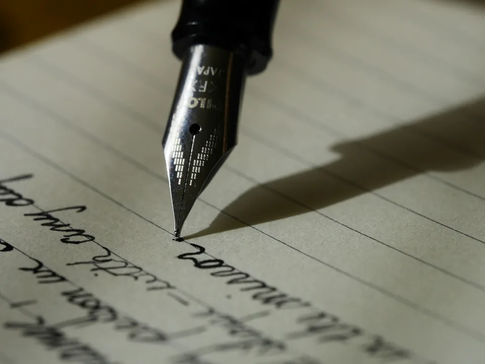A hand writing on lined paper with a fountain pen