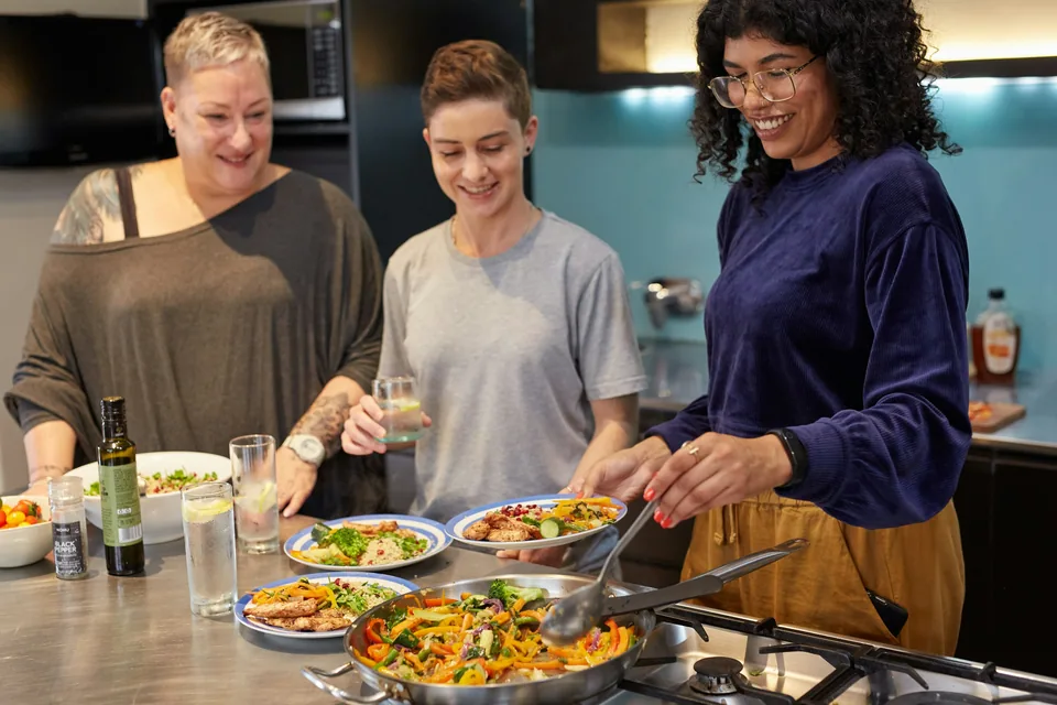 Three people preparing plates of food together in a kitchen